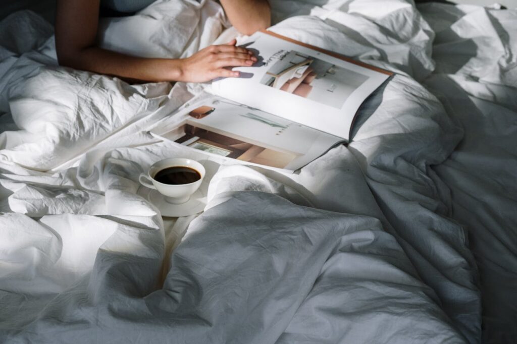 Mensch im Bett mit Kaffe und Buch unter einer Decke